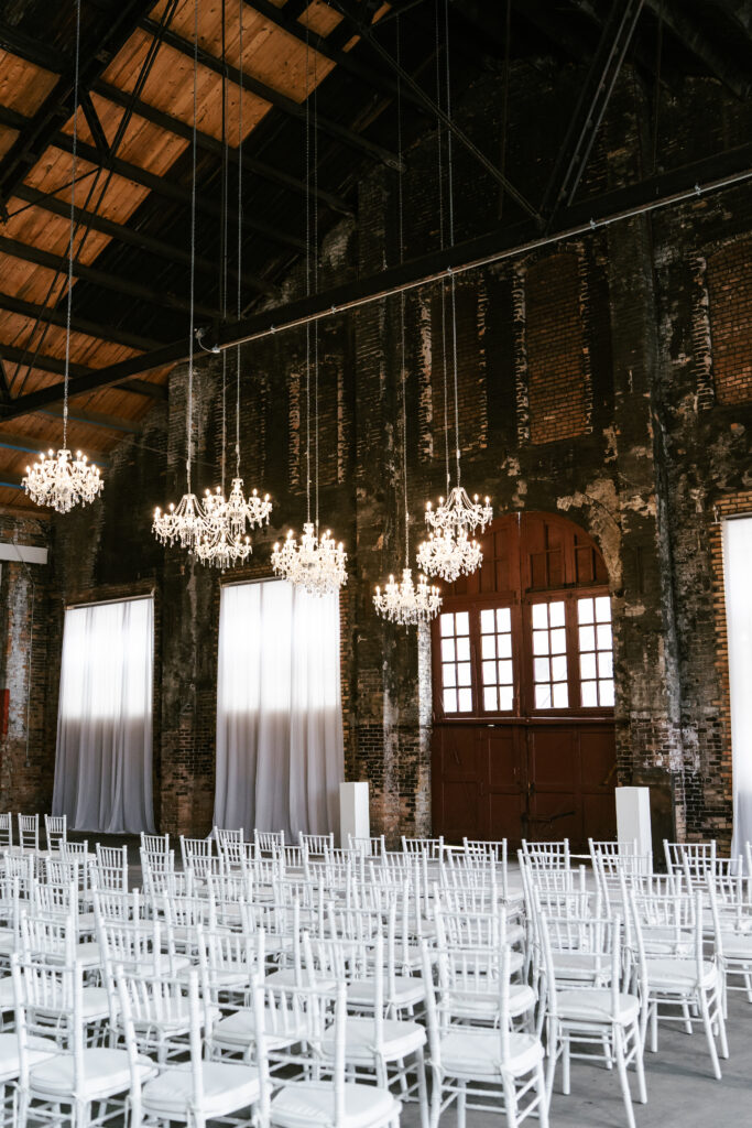 Another view of a ceremony location with red doors, white chairs, and vintage chandeliers