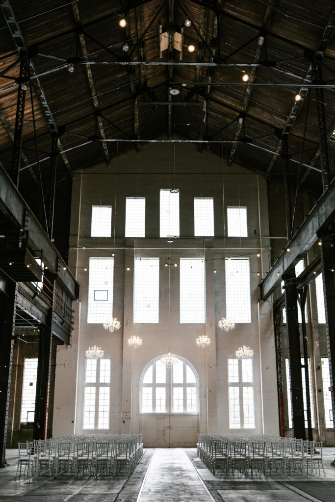 Large historic ceremony location with tall ceilings, white bricks, and white chairs